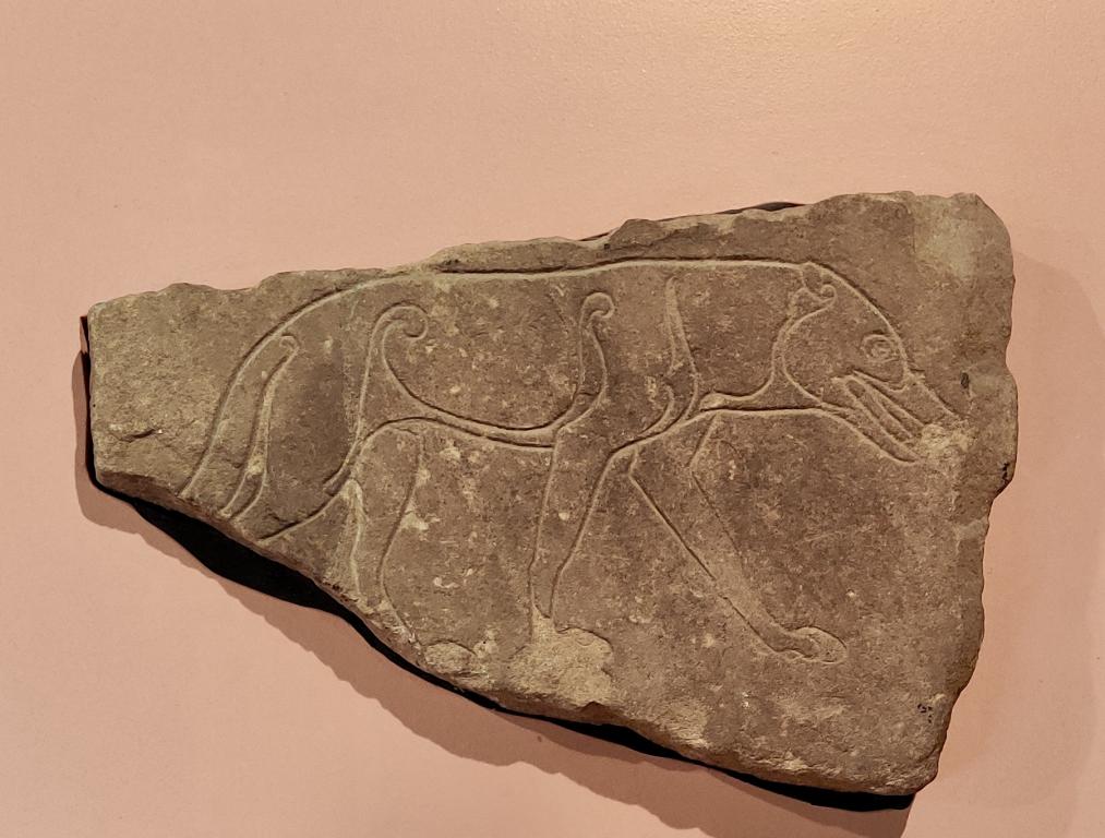 A grey stone slab is anchored against a pale orange background. The stone has an elaborate carving of a wolf carved into its surface.
