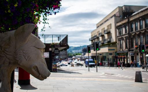 View north onto Bridge Street, Inverness. A carved stone sculpture of a dog appears on the left hand side of the image. Shop buildings line both sides of the street.