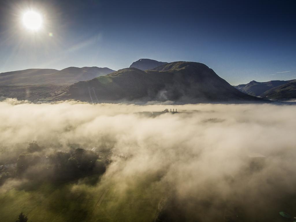 Ben Nevis rising out of the mist which covers the landscape below. The sun is shining brightly in the top left corner of the image