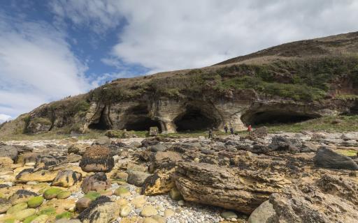 stone caves are set into the side of a mountain with a rocky beach below