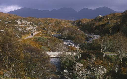 Looking Over To A Couple Walking On A Single Track Road By The Edge Of The River Inver Near Lochinver, With The Mountains Of The Quinag, Sutherland District