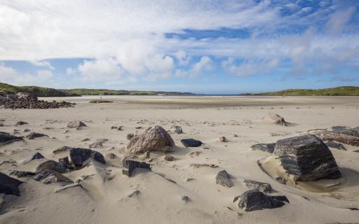 Uig Sands, Isle of Lewis. Large boulders strewn the sandy beach in the bottom half of the image. A light blue sky with large white clouds takes up the top 25% of the image