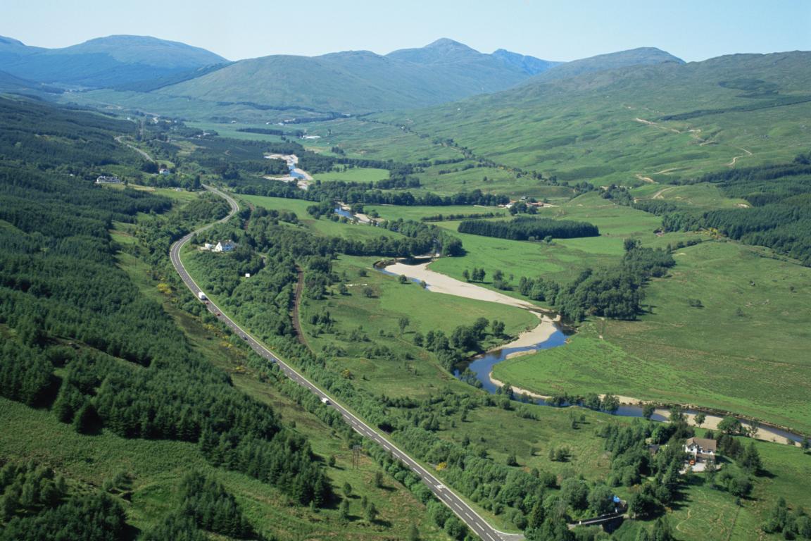 Overlooking a green valley at Strath Fillan. A main road, the A82, runs on the left hand side of the image, flanked by a wooded area on the left hand side