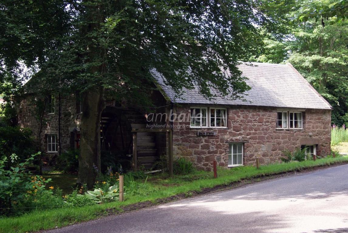 Photograph of Millnain Mill, Blairninich. The building is made of red brick with a grey slate roof. A large tree grows next to the mill on the left hand side of this image