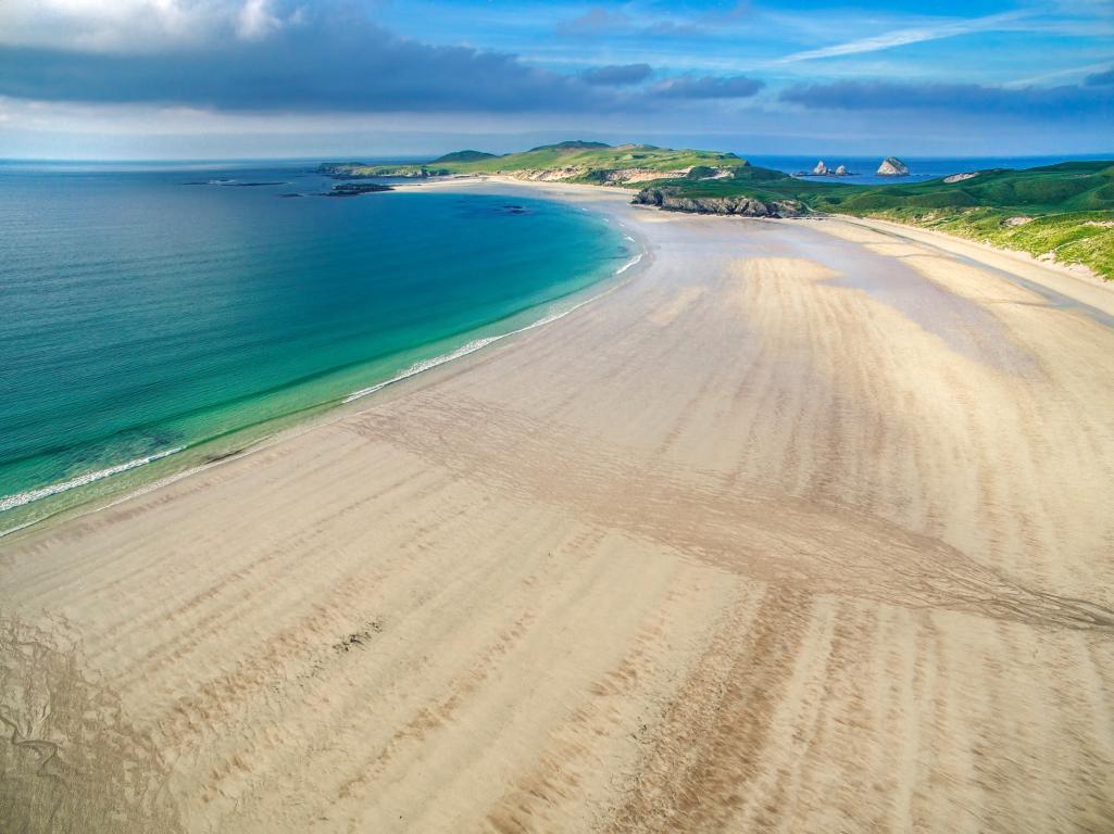 A large stretch of yellow sand swathes northwards, meeting the green-blue waters of the sea in the top left of the image