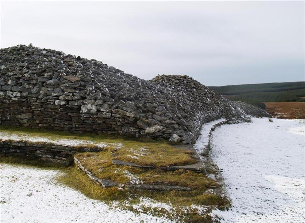 A grey stone cairn, Camster Long Cairn, atop snowy ground in Camster, Caithness