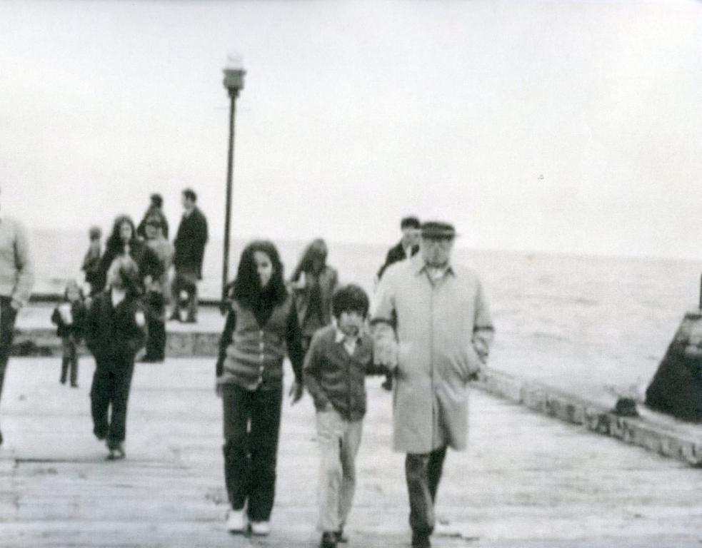A black and white image of Charlie Chaplin and his family, center, walking down Nairn pier