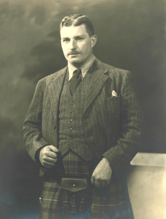 A sepia portrait of Dr Charles Ferguson. Dr Ferguson has a slicked down brown hair and a moustache. He is wearing a tweed west and jacket and a kilt with a sporran.