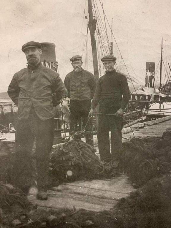 An archive image showing fishermen from Nairn standing on a pier walkway, next to nets gathered in heaps