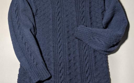 A navy, knitted gansey with detailed patterns weaved into the garment