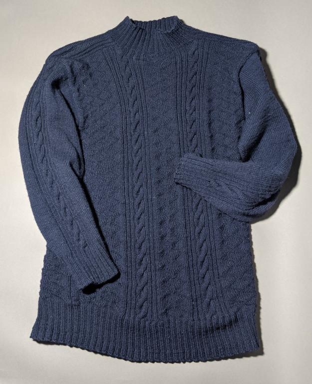 A navy, knitted gansey with detailed patterns weaved into the garment