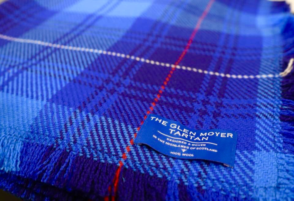 Close up image of Glen Moyer tartan - consisting of shades of light and dark blue with a single thread of red running through the cloth