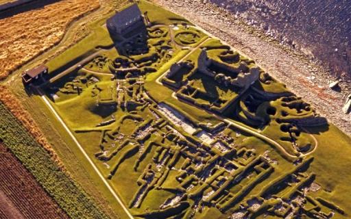 Overhead view of Jarlshof prehistoric and Norse settlement on the coast. Green linear earthworks are visible over the whole site