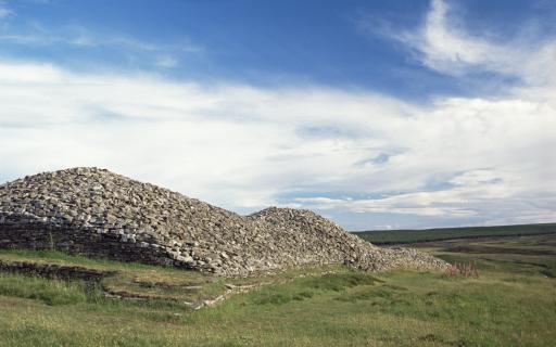 The Long Cairn, Grey Cairns of Camster, Caithness sitting atop a grassy landscape under a blue sky strewn with clouds