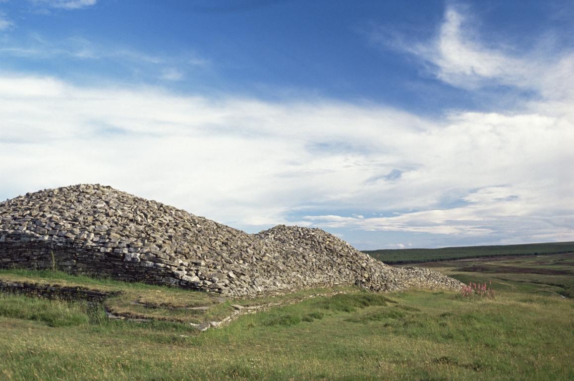 The Long Cairn, Grey Cairns of Camster, Caithness sitting atop a grassy landscape under a blue sky strewn with clouds