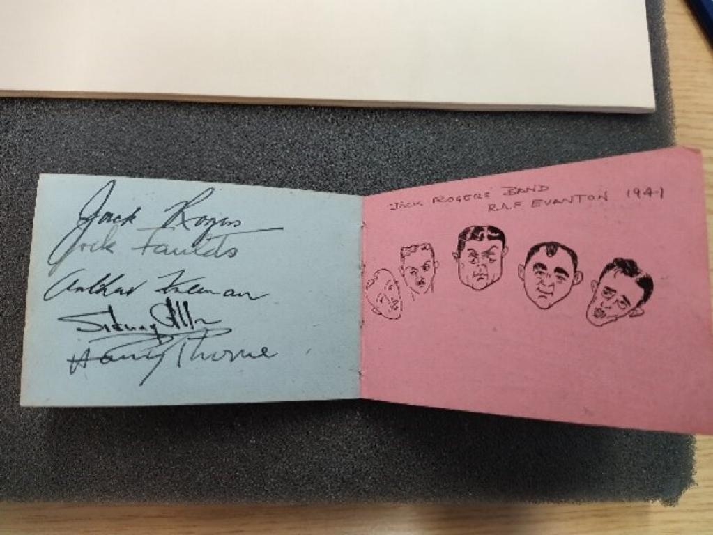 The inside of an autograph book. The left page contains the signatures backed by blue card. The right page, on red card, reads 'Jack Rogers Band RAF Evanton 1941' with cartoon sketches of band members