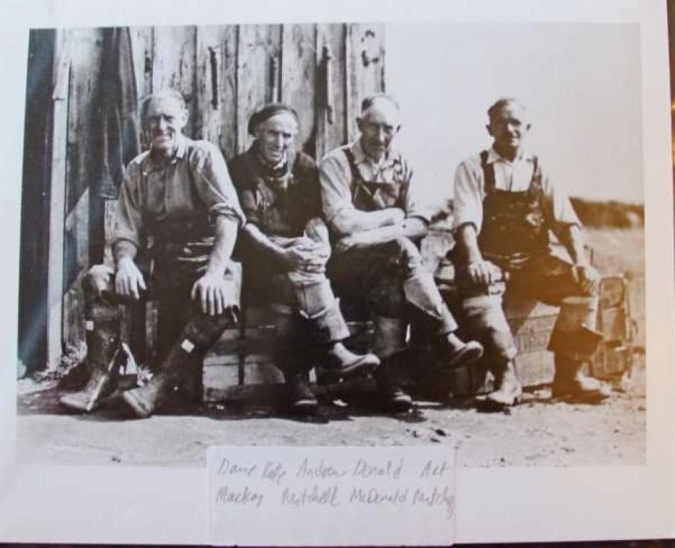 Black and white image showing four fishermen sitting down at a bothy in Rockfield