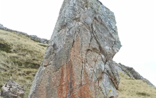 A large reddish brown boulder sitting on a grassy knoll