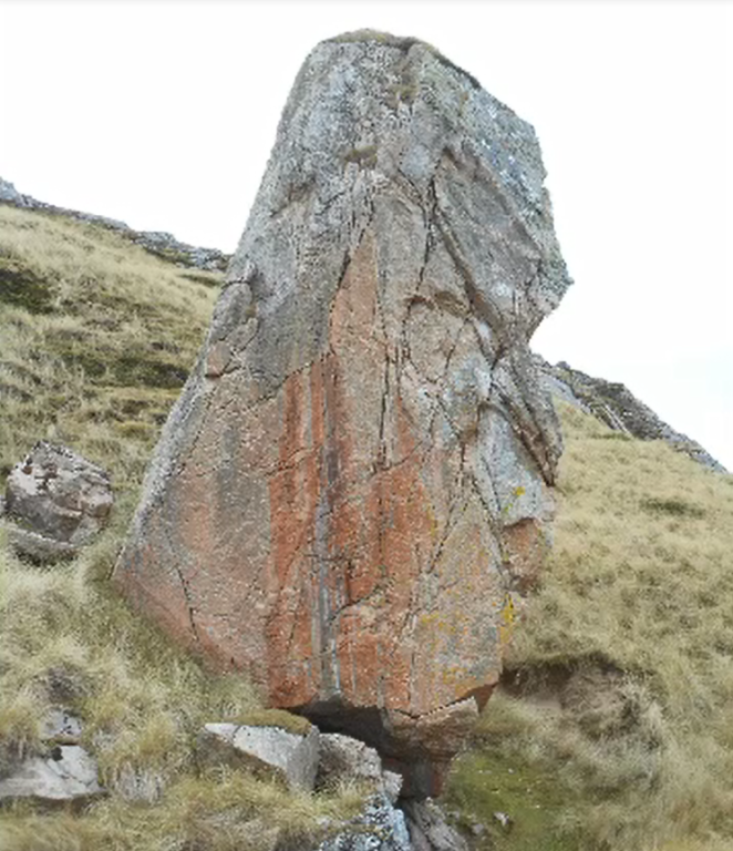 A large reddish brown boulder sitting on a grassy knoll