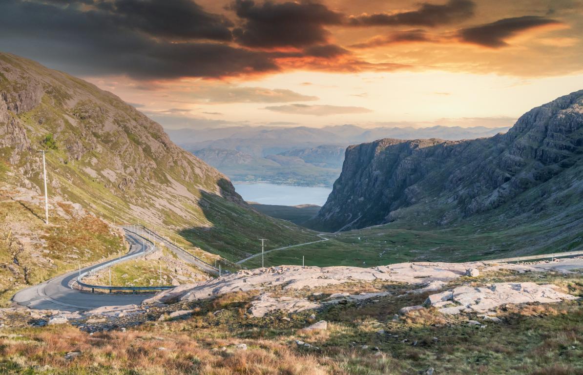 Two cliffs face each other with a single winding track road heading towards water.