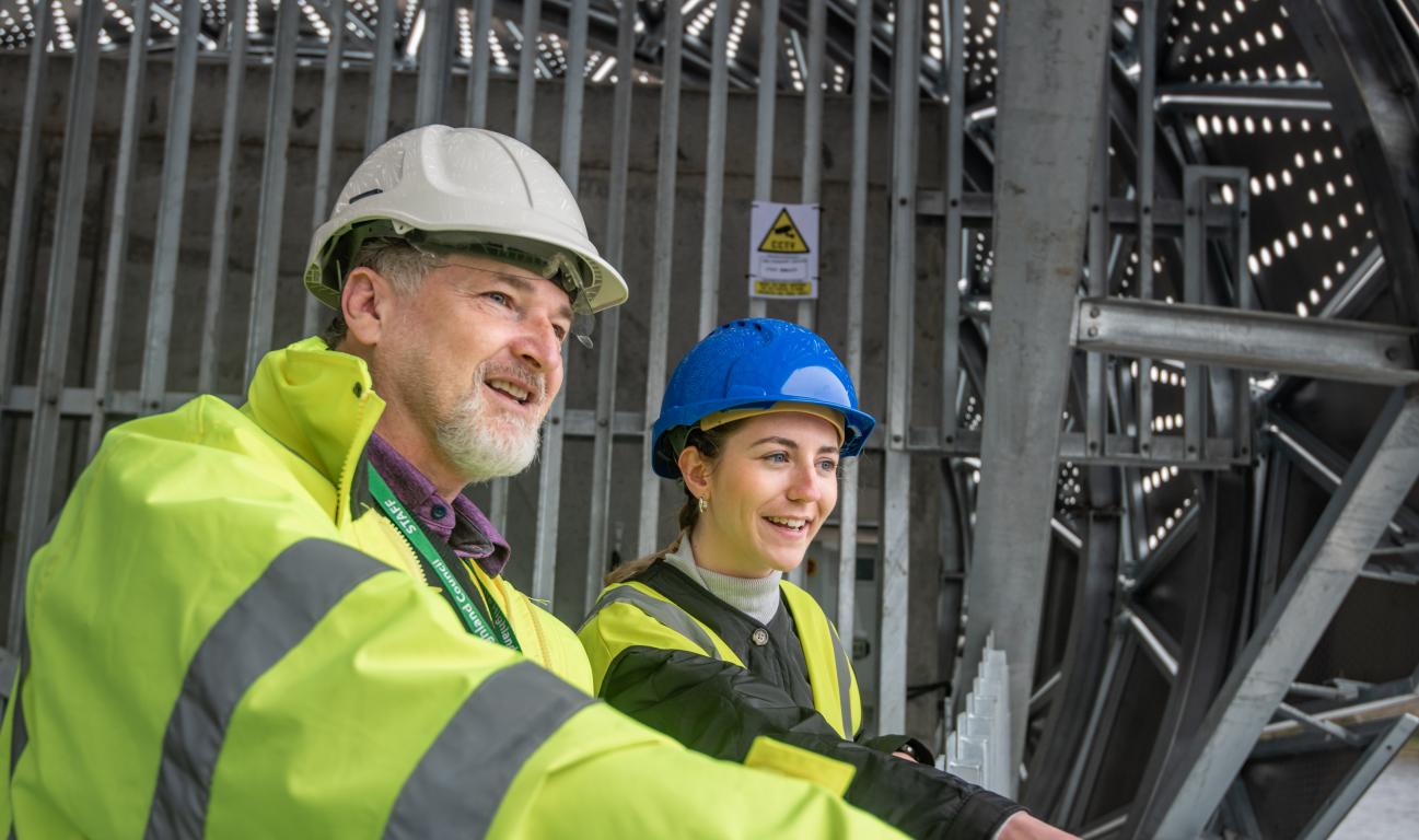 Two people in hard hats with metal gate backdrop.