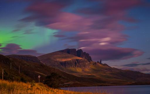 Purple, blue and green light up the sky above a rocky outcrop.
