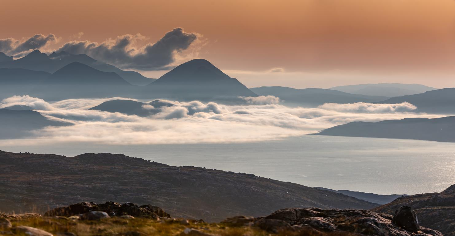 View of the Isle of Skye from the Bealach na Bà viewpoint. Low lying, long white clouds sit over the landscape.