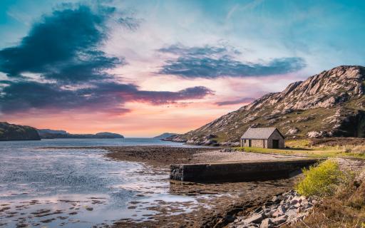Looking over onto Loch Laxford at sunset. A small stone building is seen close to a jetty in the foreground