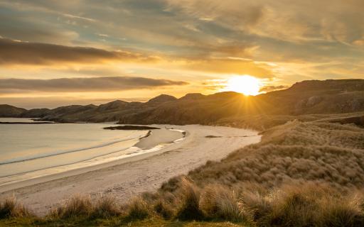 Oldshoremore bay at sunrise. Marram grass surrounds the sandy beach on the right hand side of the image