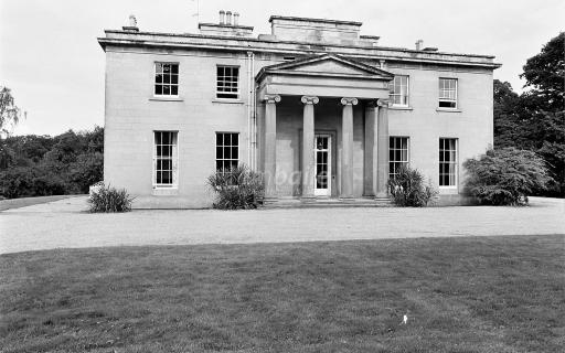 A black and white photograph showing a large brick house with four ornate columns at its entrance.