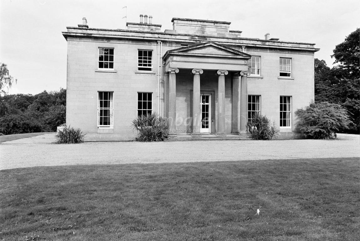 A black and white photograph showing a large brick house with four ornate columns at its entrance.