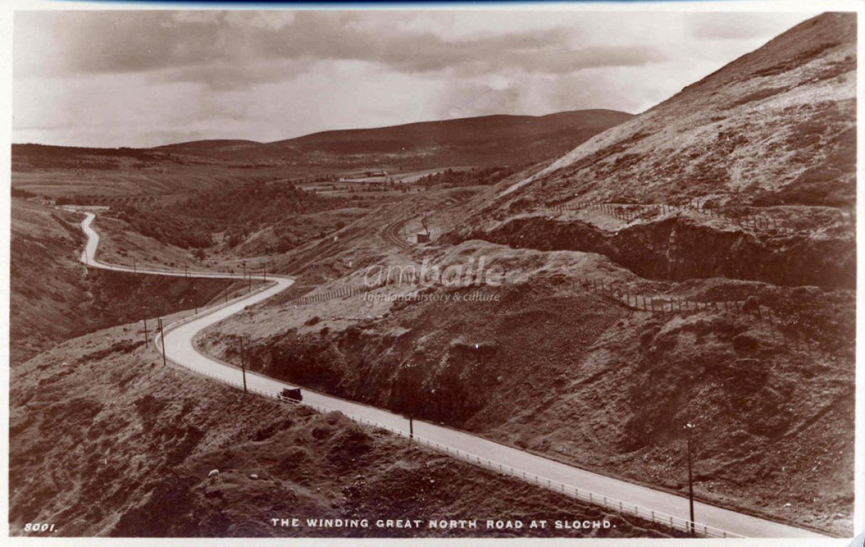 A sepia toned photograph showing a steeply sloped hillside meeting a winding road pass.