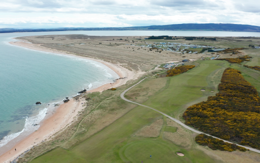 Coastline wraps around Dornoch point with green fields in the foreground and a hilly backdrop.