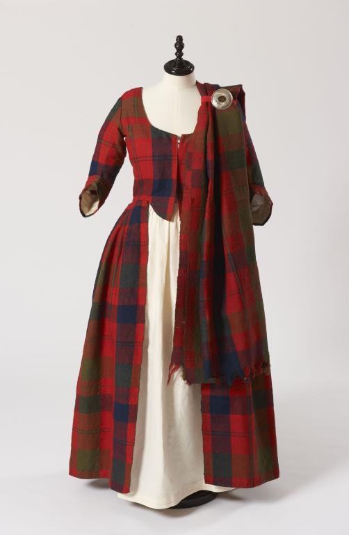 A red tartan dress on a display mannequin. The tartan is red, with black and green stripes of varying thickness running through the fabric.