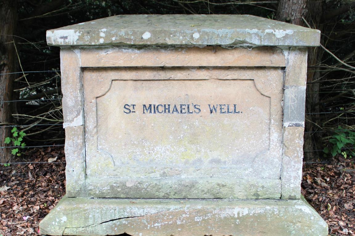 A large stone marker, with the words 'St. Michael's Well' engraved in black.