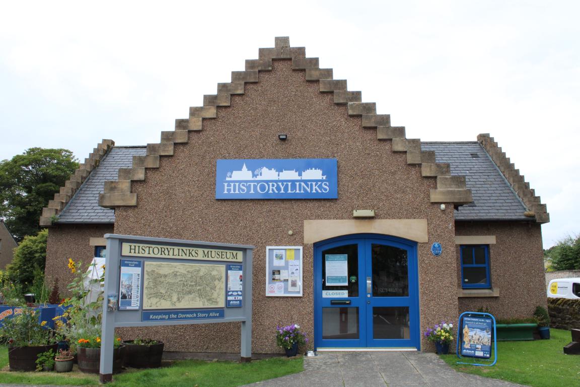 Small brown building with blue doors and windows surrounded by signs for Historylinks Museum.