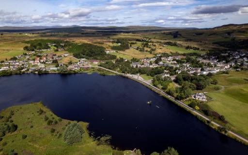 Aerial drone shot of Loch Shin and Lairg with green fields surrounding the village.