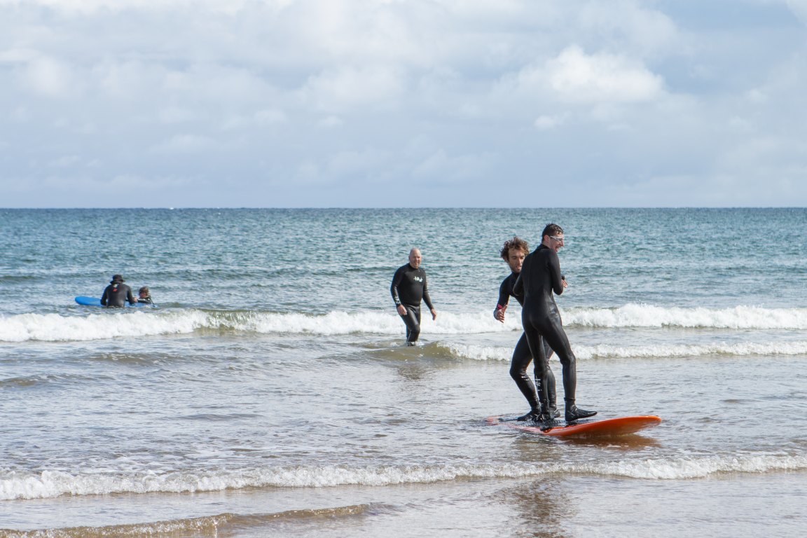 Surfers teach beginners out on small waves on beach.