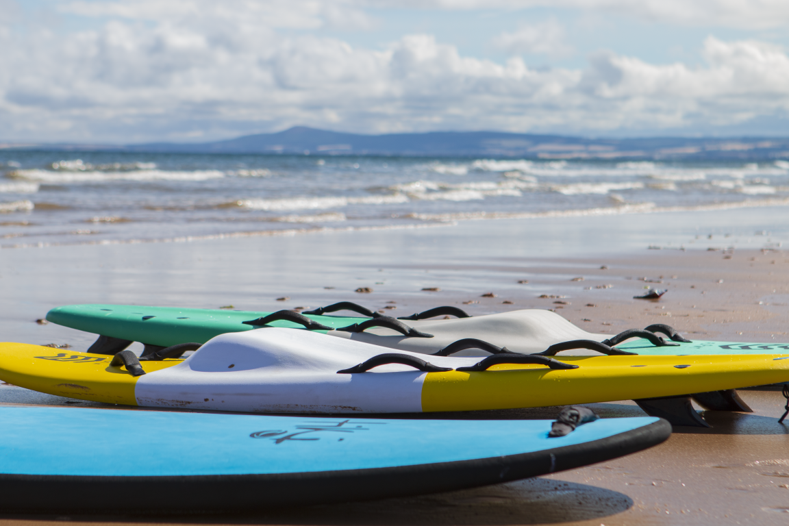Row of brightly coloured surfboards lie on sandy beach.