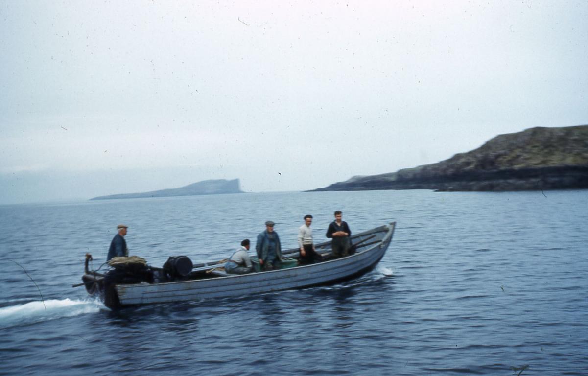 Five men in a white fishing boat which is sailing across a body of water.