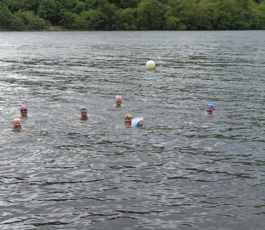 Six people swimming in colourful swimming caps in a loch.