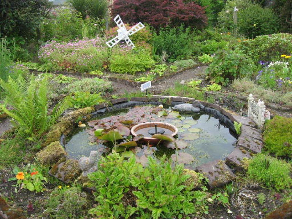 A large circular pond surrounded by green shrubs and flowers.