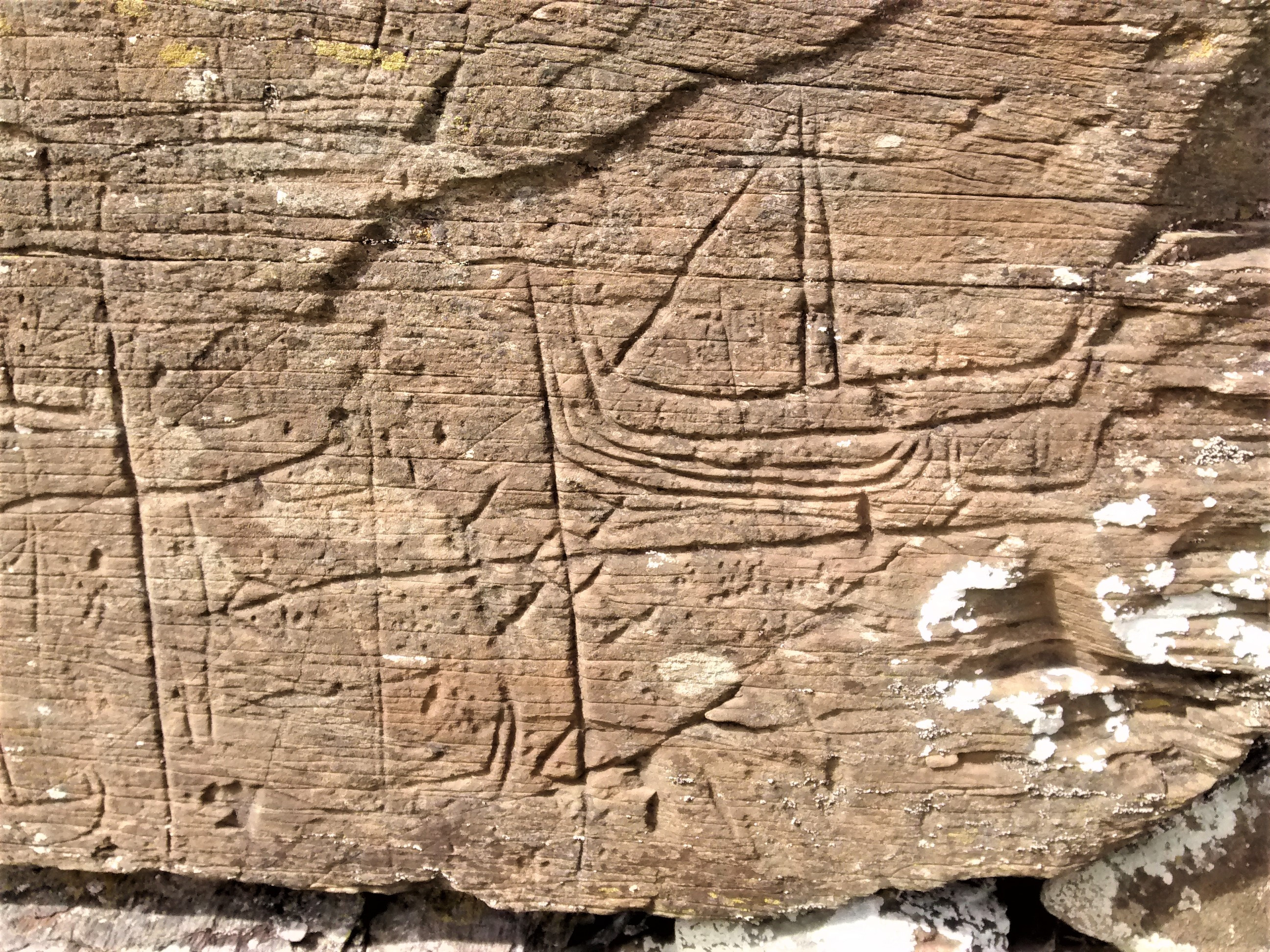Medieval graffiti on the outer wall of Kilchattan Old Parish Church. The boat has a prominent left facing sail and an end post in the shape of an animal head. Cross like motifs are also incised into the wall face.